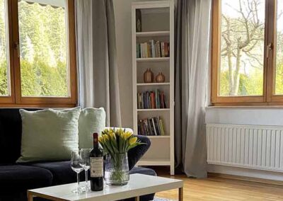 Ferienwohnung Kinzigtal: Blick ins Wohnzimmer mit zwei großen Fenstern über Eck und einer modernen Eck-Couch und Fernseher