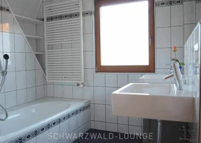 Helles Badezimmer mit Badewanne, zwei Waschbecken und großem Fenster im Ferienhaus Brestenberg.