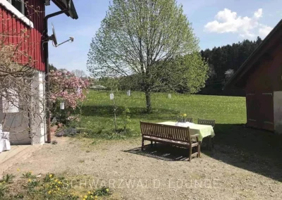 Gartenbereich am Ferienhaus Brestenberg mit Holztisch und Bänken inmitten weiter Wiesenlandschaft.