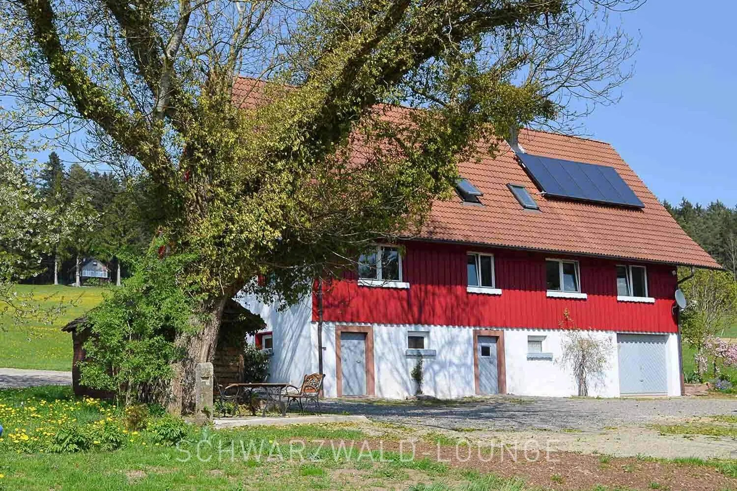 Ferienhaus Brestenberg – Außenbereich mit Spielplatz & Naturgarten Außenansicht des Ferienhauses Brestenberg mit großem Garten, Spielplatz und altem Baum.