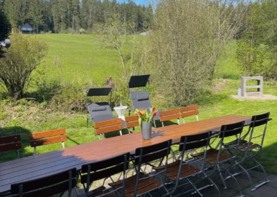 Langer Holztisch mit Gartenstühlen und Liegestühlen im Garten des Ferienhauses Brestenberg mit Blick auf Wald und Wiesen.
