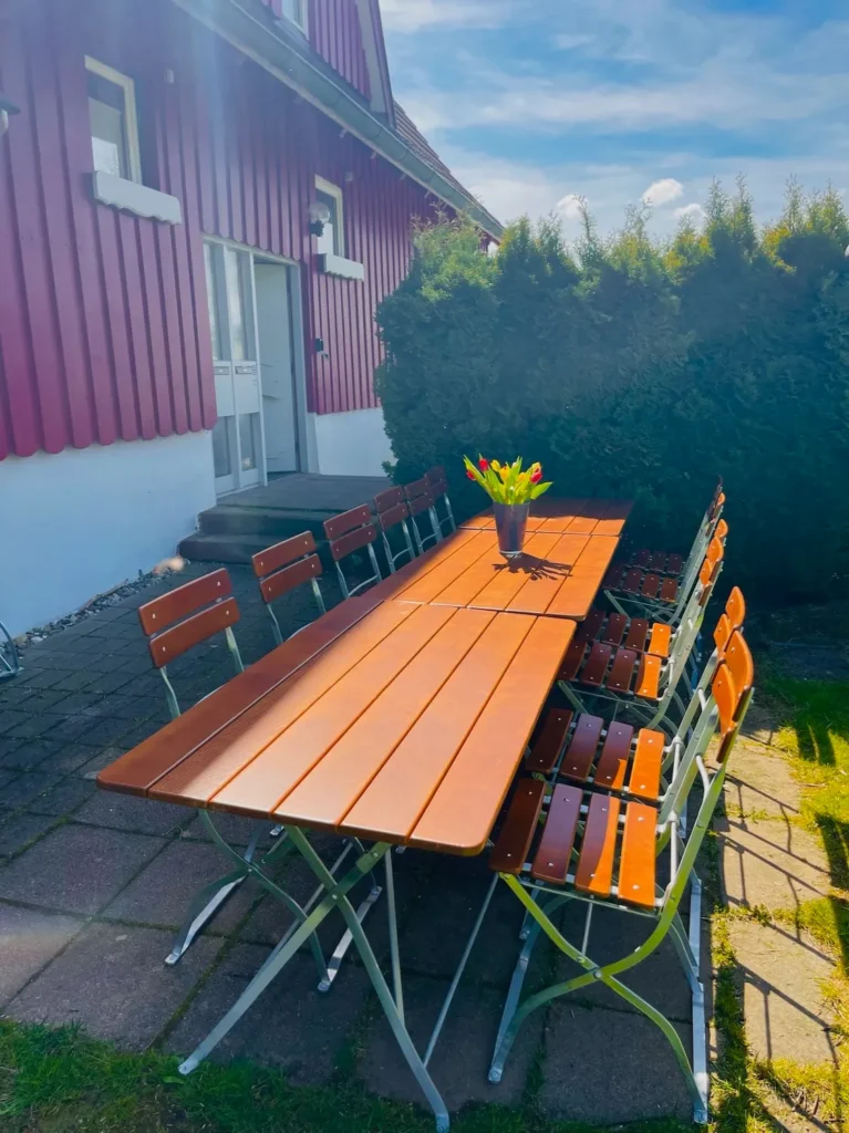 Großer Gartentisch mit Holz-Biergartenstühlen vor dem roten Ferienhaus Brestenberg im Schwarzwald.