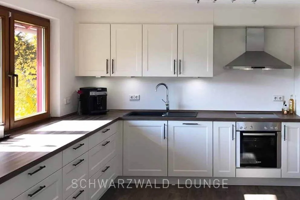Helle Landhausküche im Ferienhaus Brestenberg | Schwarzwald-Lounge Helle Landhausküche im Ferienhaus Brestenberg mit großen Fenstern, viel Arbeitsfläche und moderner Ausstattung.