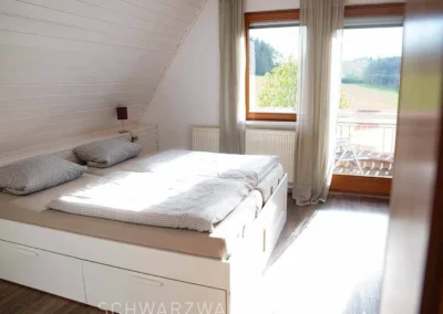 Helles Schlafzimmer im Ferienhaus Brestenberg mit Doppelbett, großen Fenstern und Zugang zum Balkon.