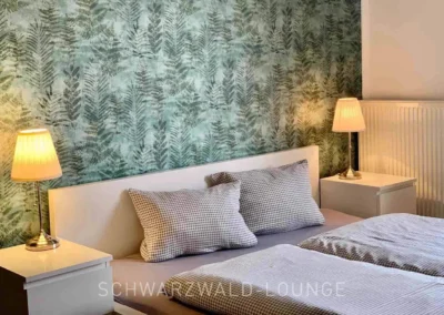 Doppelbett vor stilvoller Tapete mit warmem Licht im Ferienhaus Brestenberg.