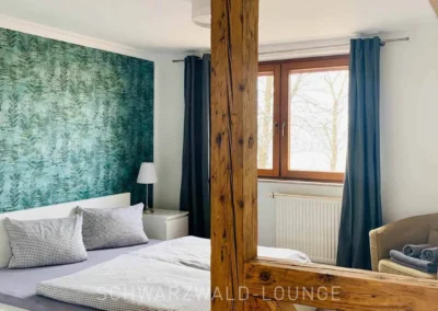 Schlafzimmer im Ferienhaus Brestenberg mit grüner Tapete, Doppelbett und sichtbarem Fachwerkbalken.