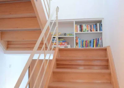 Helles Treppenhaus im Ferienhaus Brestenberg mit Bücherregal und Holztreppe.