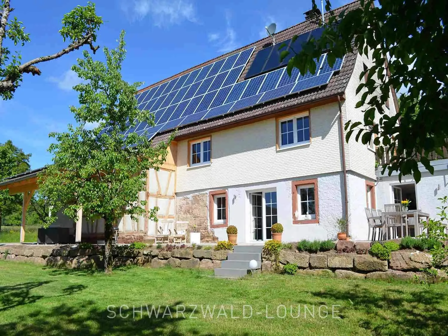 Chalet Außenansicht & Garten – Chalet Schwarzwald Lindenbuch | Schwarzwald-Lounge Außenansicht des Chalet Schwarzwald Lindenbuch mit Solaranlage, Fachwerkdetails und großem Garten.