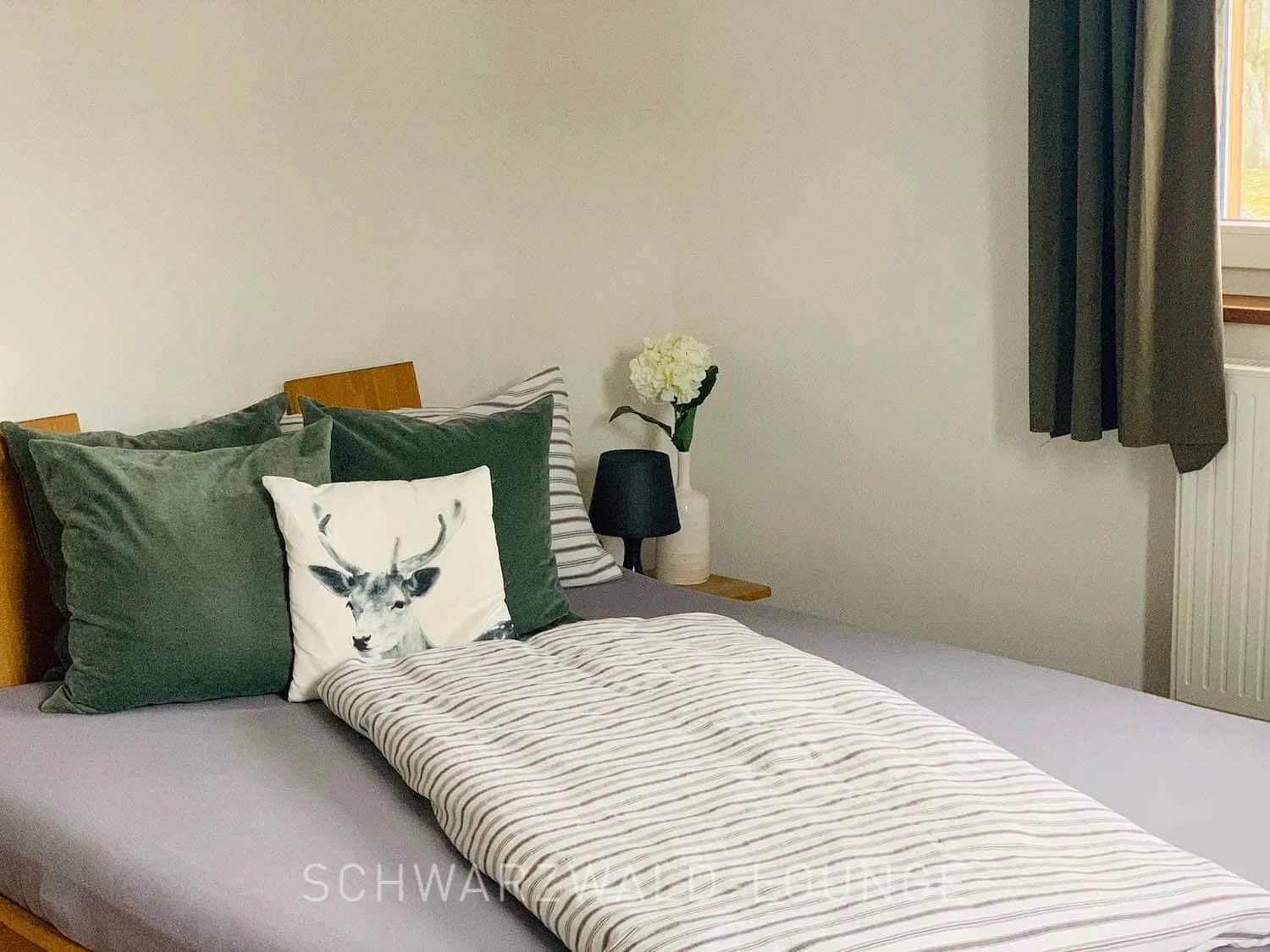 Chalet Schwarzwald – Komfortables Schlafzimmer mit Naturdesign | Lindenbuch Gemütliches Schlafzimmer im Chalet Schwarzwald Lindenbuch mit grünem Dekokissen, Hirschmotiv und Naturdeko.