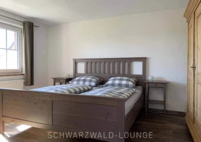 Geräumiges Schlafzimmer im Chalet Schwarzwald mit Doppelbett, grauer Bettwäsche und großem Holzschrank.
