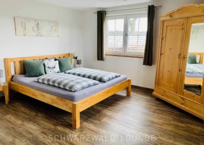 Großes Schlafzimmer im Chalet Schwarzwald Lindenbuch mit Holzbett, Kleiderschrank mit Spiegel und gemütlicher Fensterfront.