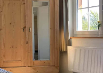 Holzschrank mit Spiegel im Schlafzimmer des Chalet Schwarzwald Ferienhauses Lindenbuch, mit Blick auf das große Fenster.