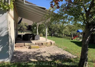 Überdachte Terrasse im Chalet Schwarzwald Lindenbuch mit Blick in den großen Garten und Spielplatzbereich.