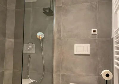 Modernes Badezimmer mit bodengleicher Dusche, grauen Fliesen und WC in der Gruppenunterkunft Schwarzwald.