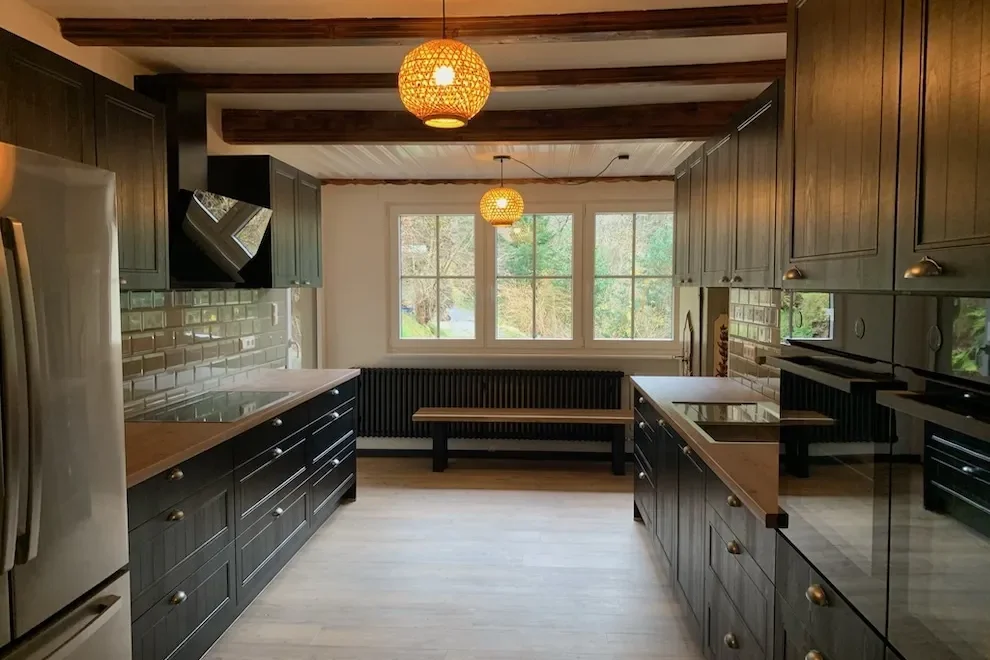 Moderne Küche im Ferienhaus Hof Busems mit dunklen Holzmöbeln, großen Fenstern und warmem Deckenlicht.