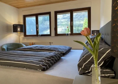 Gemütliches Schlafzimmer im Ferienhaus Hof Busems mit Doppelbett und großem Fenster mit Blick auf die Schwarzwaldlandschaft.