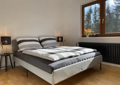 Helles Schlafzimmer mit großem Doppelbett, Fensterfront und Blick ins Grüne im Ferienhaus Hof Busems.