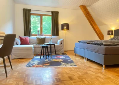 Lichtdurchflutetes Schlafzimmer mit großem Sofa, Doppelbett und farbigem Teppich im Hof Busems.