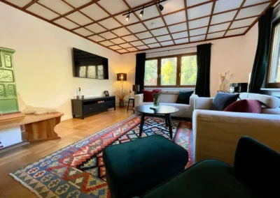 Gemütliches Wohnzimmer mit zwei Sofas, buntem Teppich, Kachelofen und großem Fenster in der Gruppenunterkunft Schwarzwald.