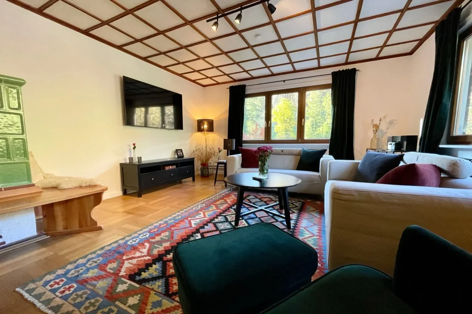 Gemütliches Wohnzimmer mit zwei Sofas, buntem Teppich, Kachelofen und großem Fenster in der Gruppenunterkunft Schwarzwald.