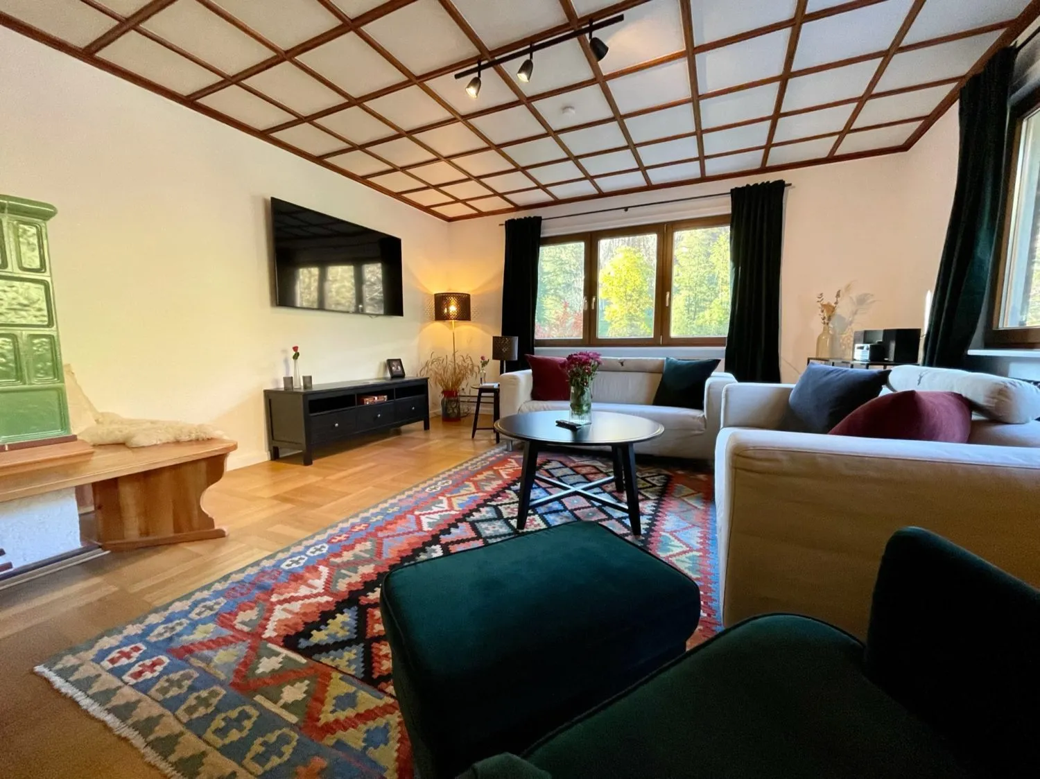 Gemütliches Wohnzimmer mit zwei Sofas, buntem Teppich, Kachelofen und großem Fenster in der Gruppenunterkunft Schwarzwald.