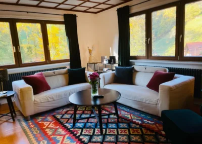 Gemütliches Wohnzimmer der Gruppenunterkunft im Schwarzwald mit zwei Sofas, Panoramafenstern und farbigem Teppich.