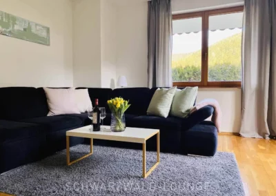 Gemütliches Wohnzimmer der Ferienwohnung Kinzigtal mit Sofa, Wein und Blick in den Garten