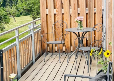 Holzbalkon mit Tisch, Stühlen und Blumen in der Ferienwohnung Ostweg im Schwarzwald.