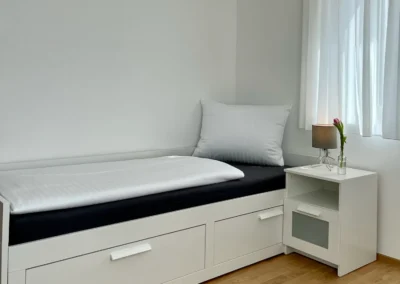 Ostweg Schwarzwald – helles Schlafzimmer mit Einzelbett und weißem Nachttisch in der Ferienwohnung Schwarzwaldlounge