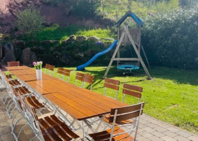 Langer Gartentisch mit vielen Sitzplätzen und Spielturm im Garten des Schwarzwald Chalet Lohmühle.