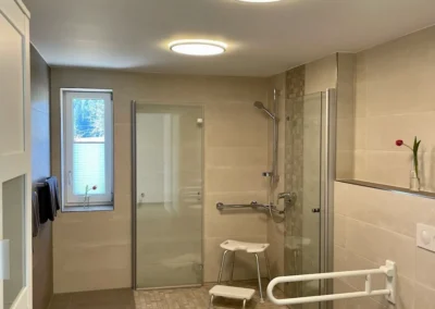 Großzügiges barrierefreies Badezimmer mit ebenerdiger Dusche, Haltegriffen und angepasster Toilette.