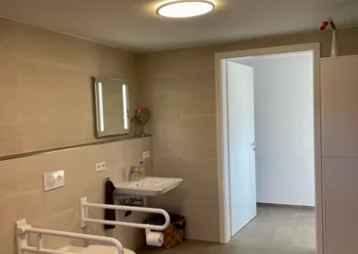 Barrierefreies Badezimmer der Ferienwohnung Westweg mit höhenverstellbarem Waschbecken und Stützgriffen an der Toilette.