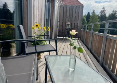 Sonniger Balkon der Ferienwohnung Westweg mit Sitzmöbeln und Blumen.