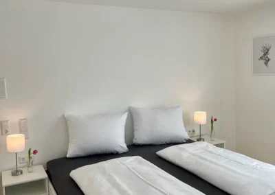 Doppelbett mit weißen Bettwaren und zwei Nachttischlampen in der Ferienwohnung Westweg im Schwarzwald.