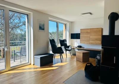 Wohnzimmer der Ferienwohnung Westweg mit Kamin, gemütlichen Sesseln und Zugang zum Balkon.