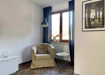 Gemütliche Leseecke mit Sessel und Fensterblick in der Ferienwohnung Bergsee im Schwarzwald.