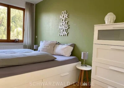 Modernes Schlafzimmer mit Doppelbett, Kommode und grüner Akzentwand im Apartment Bergsee.
