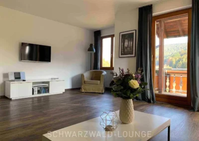 Wohnzimmer mit Sessel und Blick auf den Balkon und die Schwarzwaldberge im Apartment Bergsee.