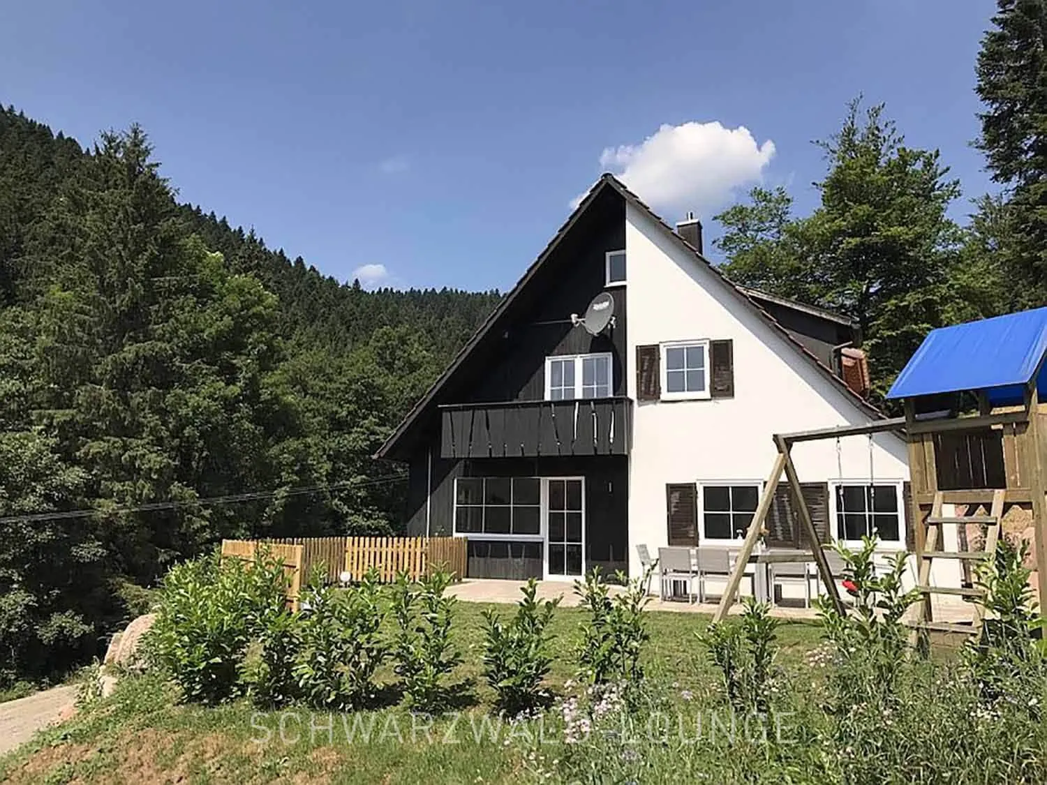 Schwarzwald Chalet Lohmühle – Außenansicht mit Garten, Spielplatz und Waldkulisse im Hintergrund.