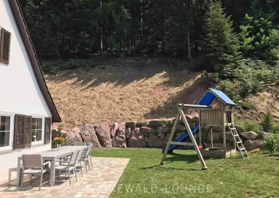 Garten des Schwarzwald Chalet Lohmühle mit Spielplatz, Rutsche und großer Terrasse mit Esstisch im Grünen.