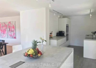 Moderne Küche im Schwarzwald Chalet Lohmühle mit Kochinsel, Obstschale und Blick in den Essbereich.