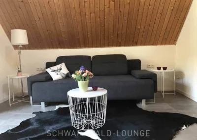 Modernes graues Sofa mit Dekokissen in der großzügigen Suite des Schwarzwald Chalet Lohmühle.
