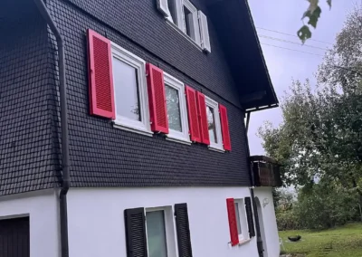 Außenansicht des Ferienhauses Tanne und Tal Relax mit schwarzen Schindeln und roten Fensterläden.