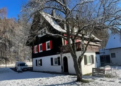 Schwarzwälder Ferienhaus Tanne und Tal Relax mit roter Fensterläden, Balkon und verschneitem Garten.