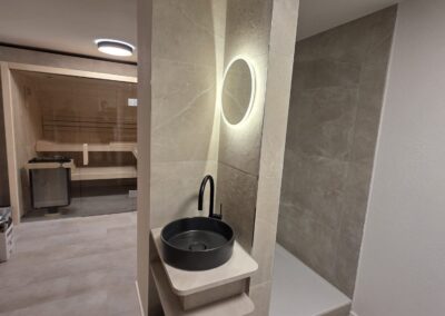 Moderner Wellnessbereich im Tanne und Tal Relax mit Waschbecken, beleuchtetem Spiegel und begehbarer Dusche.