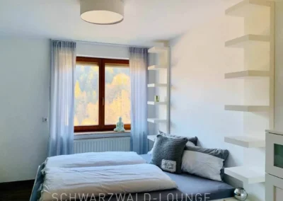 Helles modernes Schlafzimmer der Ferienwohnung Waldwiese mit großem Doppelbett und Fensterblick.
