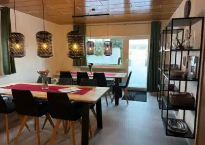 Essbereich mit Holztischen, Pendelleuchten und Terrassentür im Ferienhaus Tanne und Tal Relax.