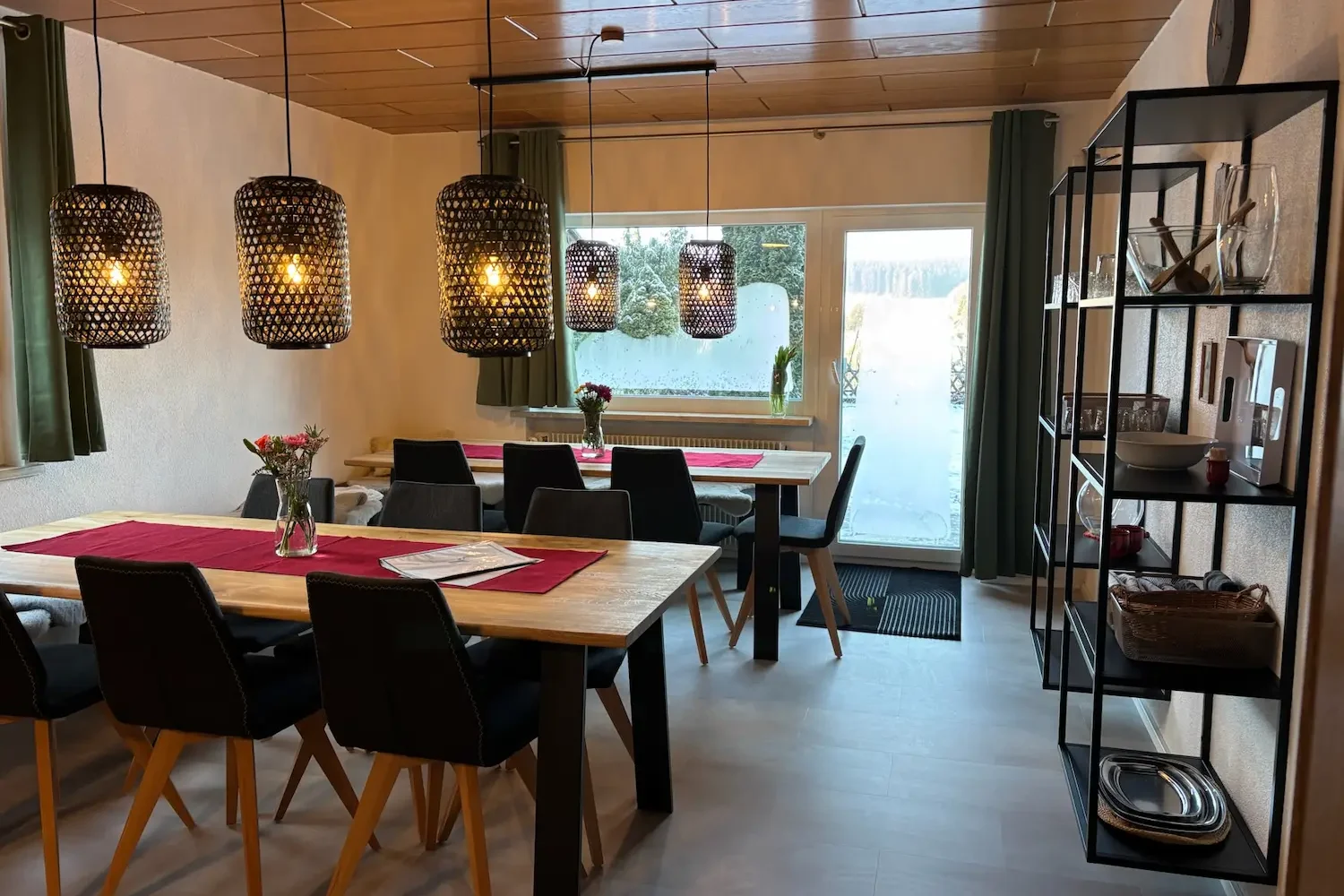 Großzügiger Essbereich mit Holztischen, Pendelleuchten, Regal und Terrassenzugang im Ferienhaus Tanne und Tal Relax im Schwarzwald.