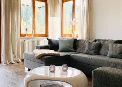 Wohnzimmer der Ferienwohnung Waldwiese mit großem Sofa und Panoramafenstern zur Schwarzwaldlandschaft.