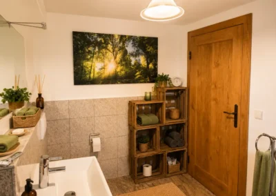 Gemütliches Badezimmer mit Naturstein-Optik und grünen Handtüchern im Refugium am Ursprung